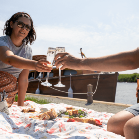 Couple raising a toast whilst enjoying a picnic by the Norfolk Broads