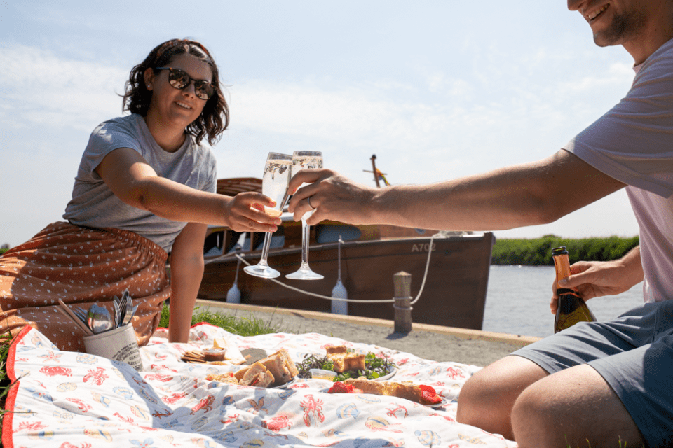 Couple raising a toast whilst enjoying a picnic by the Norfolk Broads